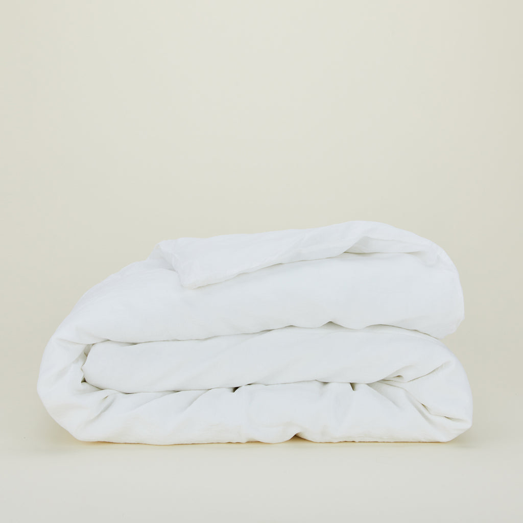 White linen duvet cover folded on a neutral studio background.